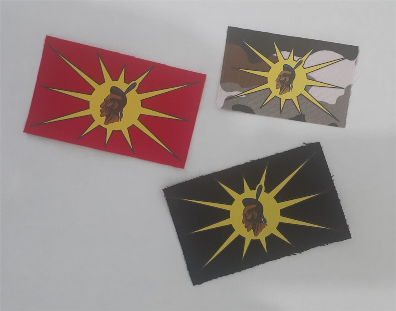 May include: Three fabric patches with a Native American profile design in the center of a yellow sunburst. The patches are on a white background. The patches are red, camouflage, and black.