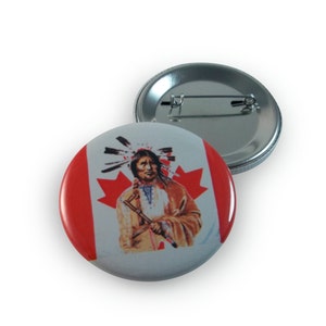 May include: A round button with a glossy finish features a depiction of a Native American man wearing a headdress and holding a staff. The background is a stylized Canadian flag with a red maple leaf.