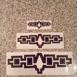 May include: Three white stickers with a black and purple geometric design. The design features a central diamond shape with squares on either side. The stickers are different sizes.