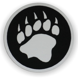 May include: A black and white circular patch with a white bear paw print in the centre. The paw print has five toes and claws.