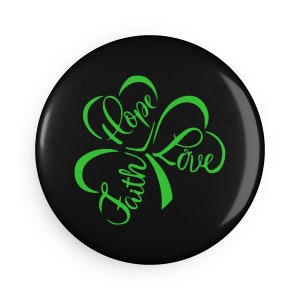 May include: A black button with a green shamrock design. The shamrock has the words "Faith", "Hope", and "Love" written inside it.