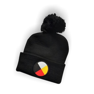 May include: Black beanie with a pom pom on top and a circular patch with four colors: black, red, yellow, and white. The patch is a symbol of the four directions.