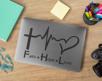 Könnte beinhalten: Ein grauer Laptop mit einem schwarzen Vinyl-Aufkleber mit einem Kreuz, einem Herzschlag und einem Herzen mit dem Text "Faith. Hope. Love".