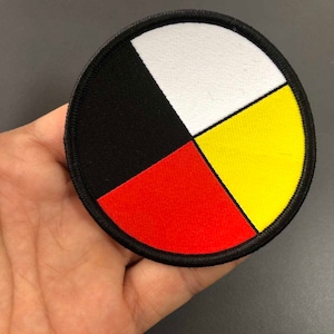 May include: A round, embroidered patch with a black, white, red, and yellow design. The design is divided into four sections, each a different colour. The patch is surrounded by a black border.