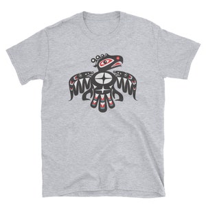 May include: A grey t-shirt with a black and red stylized image of a bird with a large eye and a red beak. The bird is surrounded by geometric patterns.