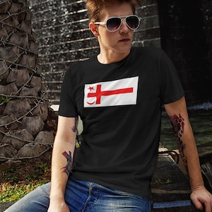 May include: A black t-shirt featuring a white and red flag design. The flag depicts a red cross and a crescent moon.