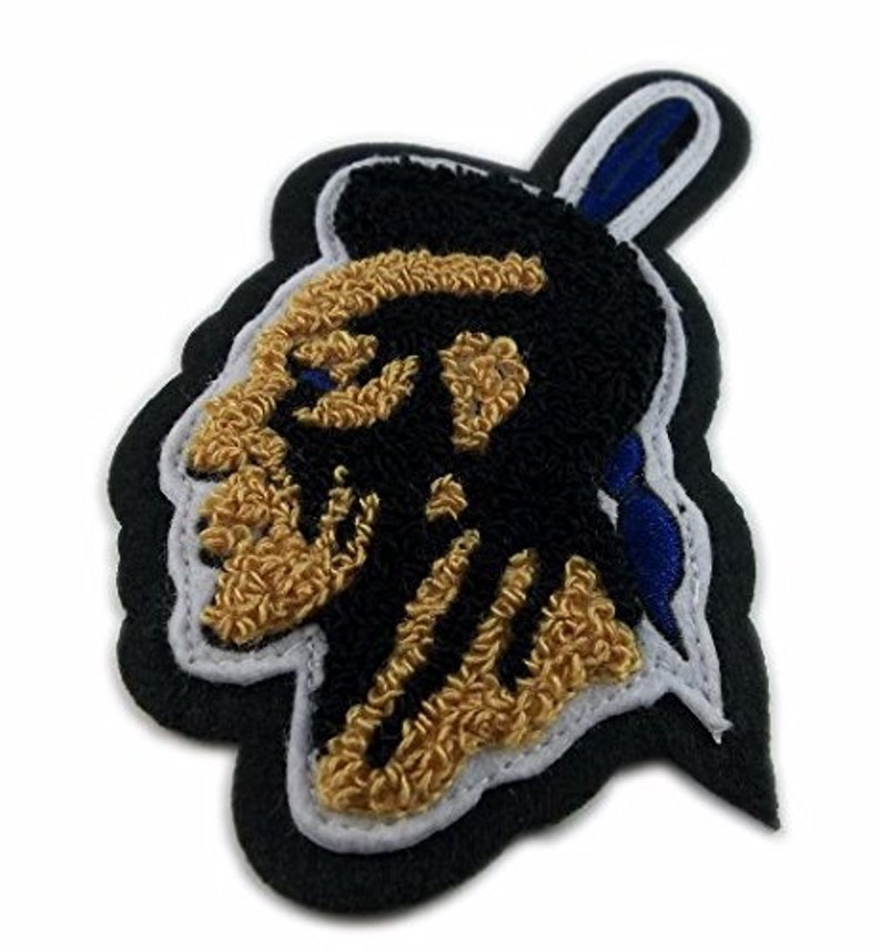 May include: A black and gold embroidered patch with a stylized image of a Native American chief's head. The patch has a blue and white border.