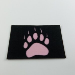 May include: A black patch with a pink bear paw print.