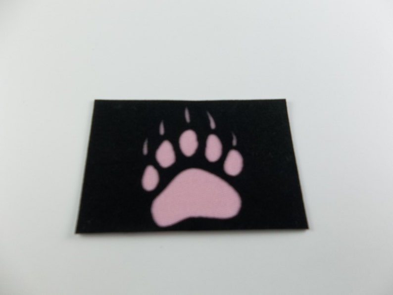May include: A black patch with a pink bear paw print.