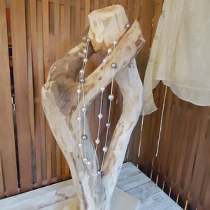 May include: A wooden jewelry stand with a natural, weathered finish. A pearl necklace with light pink and gray pearls is draped around the stand.