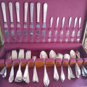 May include: A set of silverware in a wooden case with a burgundy velvet lining. The silverware includes forks, knives, spoons, and butter knives. The set is arranged in rows and is ready to be used.