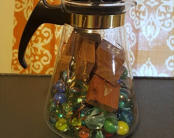 Vintage Pyrex coffee pot filled with vintage marbles and wooden game pieces.