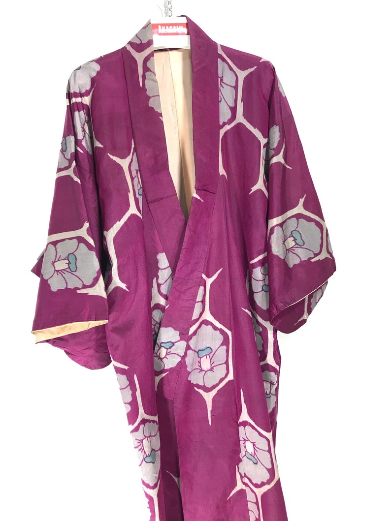May include: A purple kimono with a white and blue floral pattern. The kimono is hanging on a hanger.