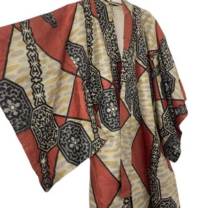 Peut inclure: Un kimono vintage avec un motif géométrique dans les tons de rouge, beige, noir et or. Le kimono présente un motif en forme de losange et de chaîne. Le vêtement est suspendu à une chaîne sur fond blanc.