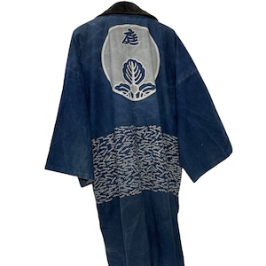 Op de afbeelding: Een donkerblauwe Japanse kimono met een wit geborduurd ontwerp op de rug. Het ontwerp bevat een cirkel met een gestileerde bloem en het Japanse karakter "寿" (ju) wat lang leven betekent. De kimono heeft een zwarte kraag en een patroon van witte zwaarden op de onderste helft.