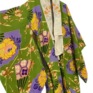 May include: A green kimono with a floral pattern featuring yellow, purple, and orange flowers. The kimono has a white collar with embroidered flowers.