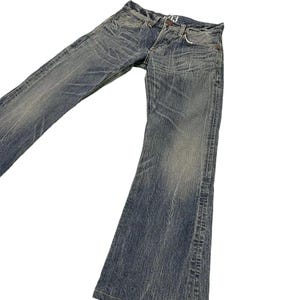 May include: Faded blue denim jeans with a flared leg design. The jeans have a worn, distressed look with visible fading and subtle whiskering details. The jeans have a classic five-pocket design and a button and zipper closure.