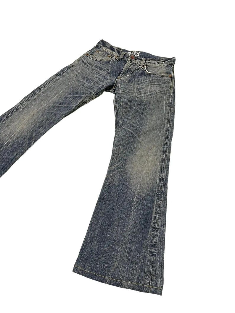 May include: Faded blue denim jeans with a flared leg design. The jeans have a worn, distressed look with visible fading and subtle whiskering details. The jeans have a classic five-pocket design and a button and zipper closure.