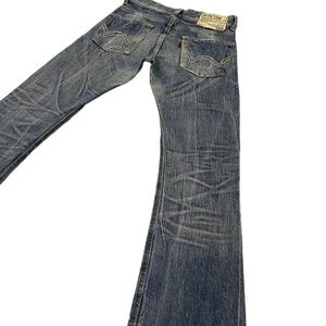 May include: Faded blue denim jeans with a flared leg design. The jeans have a worn appearance with visible fading and distressing. Features include classic five-pocket styling, a red tag, and a leather patch on the back. The jeans are laid flat against a white background.