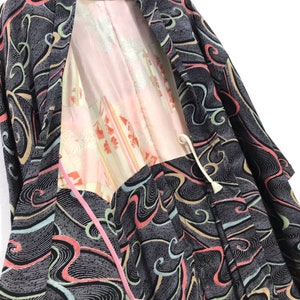 Könnte beinhalten: Ein schwarzer und grauer japanischer Kimono mit einem bunten Wellenmuster. Der Kimono ist mit einem rosa und weißen Stoff mit Blumenmuster gefüttert. Der Kimono hat eine Bindekordel mit einem Quasten.