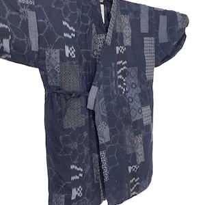 May include: Dark blue quilted kimono-style jacket with a patchwork design. The jacket features various geometric and abstract patterns in shades of gray and blue. It has wide sleeves and a tie belt.