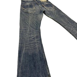 May include: Blue denim jeans with a flared leg design. The jeans have classic five-pocket styling, a button and zipper closure, and a faded wash. The back pockets feature a signature stitch detail. A small tag is visible on the back.