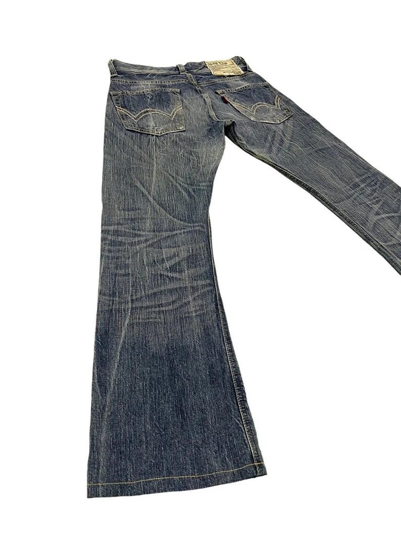 May include: Blue denim jeans with a flared leg design. The jeans have classic five-pocket styling, a button and zipper closure, and a faded wash. The back pockets feature a signature stitch detail. A small tag is visible on the back.