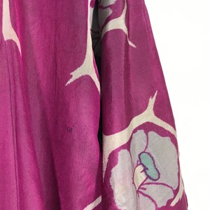 May include: A close-up of a purple silk kimono with a white floral pattern. The kimono has a large white flower with a teal center.