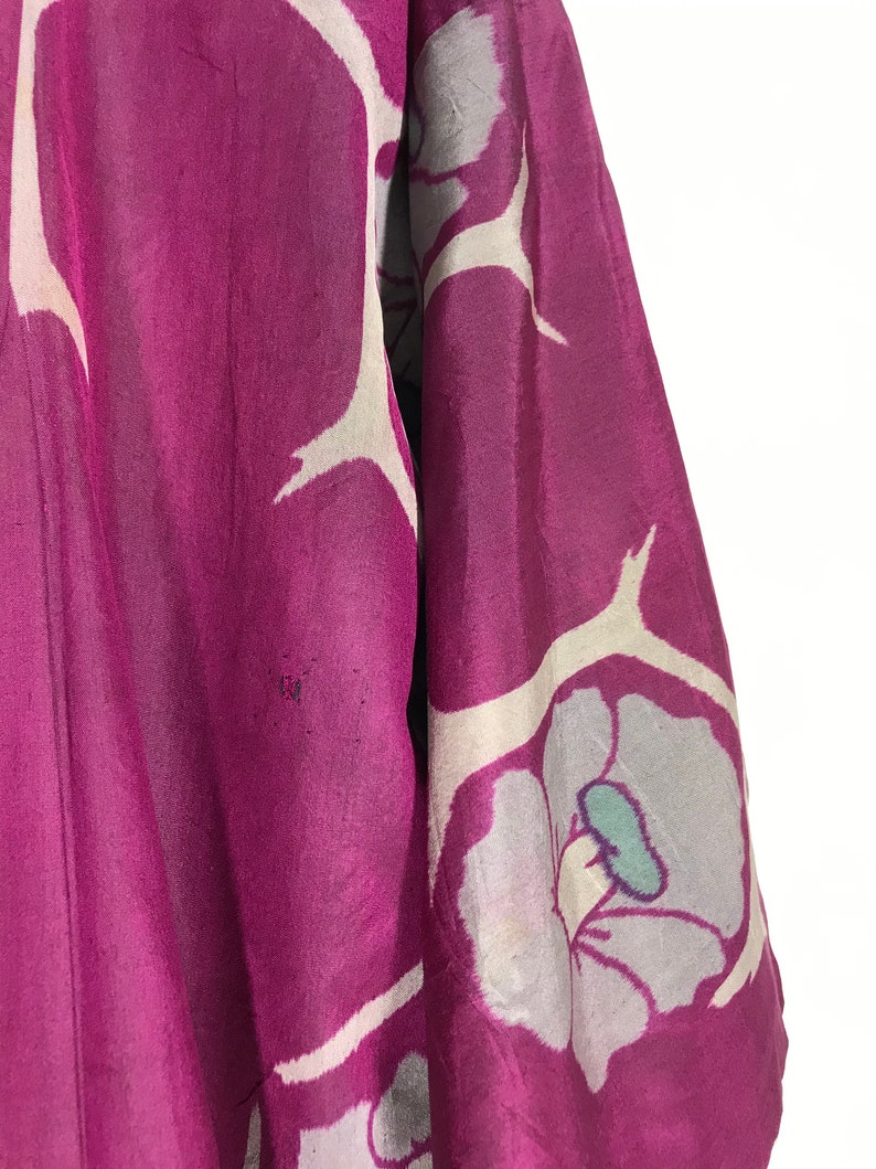 May include: A close-up of a purple silk kimono with a white floral pattern. The kimono has a large white flower with a teal center.