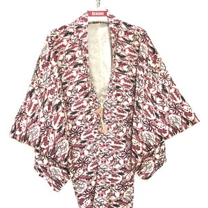 May include: A white and pink patterned Japanese kimono with black accents. The kimono is hanging on a hanger with a red tag that says "AKAGAMI".