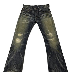 Puede incluir: Vaqueros de mezclilla de lavado oscuro con un dise&ntilde;o desgastado y descolorido. Los vaqueros tienen una abertura de pierna acampanada y presentan ligeros desgastes en las rodillas y los muslos. Los vaqueros tienen un dise&ntilde;o cl&aacute;sico de cinco bolsillos.