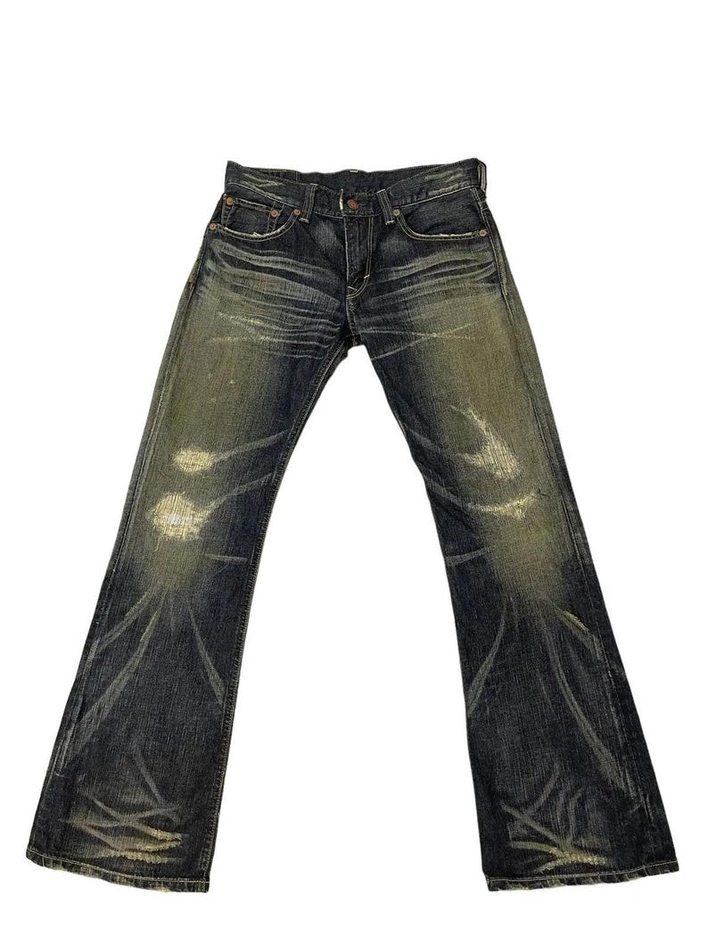 Puede incluir: Vaqueros de mezclilla de lavado oscuro con un dise&ntilde;o desgastado y descolorido. Los vaqueros tienen una abertura de pierna acampanada y presentan ligeros desgastes en las rodillas y los muslos. Los vaqueros tienen un dise&ntilde;o cl&aacute;sico de cinco bolsillos.
