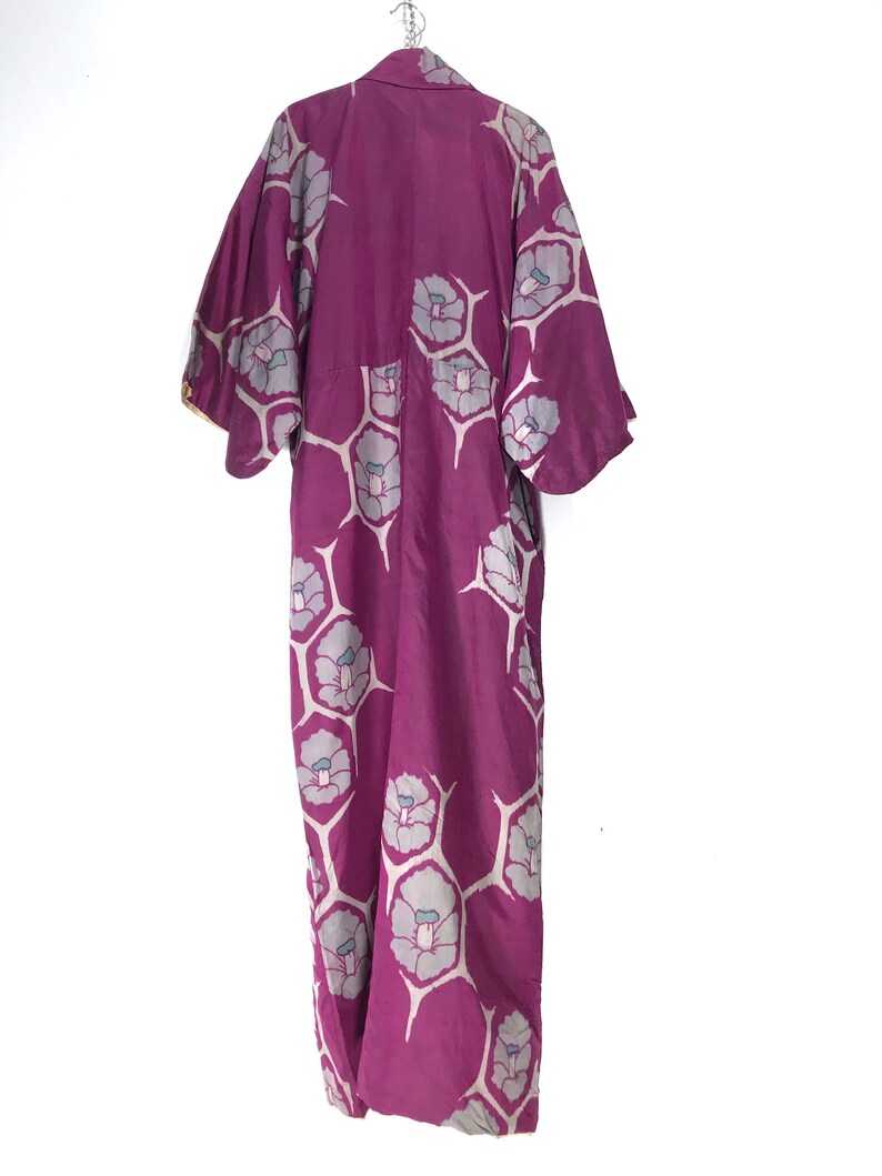 May include: A long, purple silk kimono with a floral pattern. The flowers are white with a light blue center and are arranged in a repeating pattern.