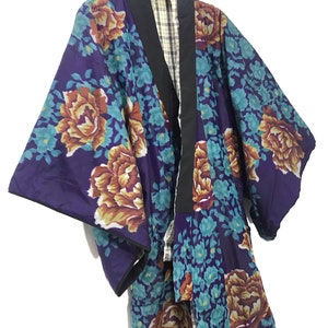 May include: A purple and teal floral patterned kimono with a black collar and a plaid lining. The kimono is hanging on a hanger.