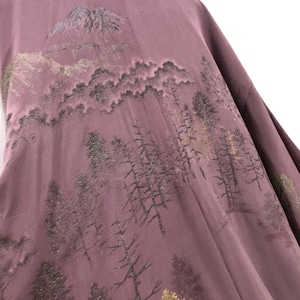 Puede incluir: Un kimono de seda malva con una escena de montaña y bosque bordada en hilo negro y dorado.
