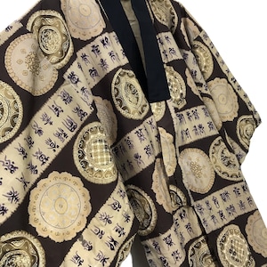 May include: A brown and beige kimono with a black collar. The kimono is decorated with a repeating pattern of gold circles and purple script.