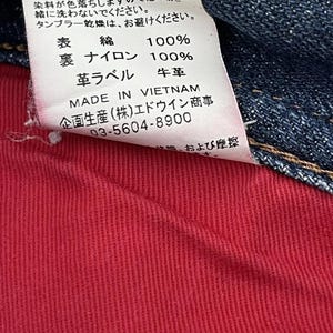 Puede incluir: Primer plano de una etiqueta de ropa con texto en japon&eacute;s e ingl&eacute;s. La etiqueta est&aacute; adherida a tela vaquera y tela roja. La etiqueta incluye instrucciones de lavado, composici&oacute;n de la tela y el texto "MADE IN VIETNAM".