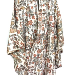 May include: A cream-colored kimono with a floral pattern in shades of orange, brown, and gray. The kimono features a wide collar and long sleeves. The fabric is patterned with flowers, vases, and other botanical elements.
