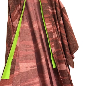May include: A red and brown patterned kimono with a lime green lining. The kimono is folded and hung on a hanger.