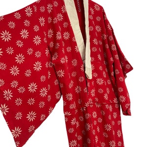 May include: A red kimono with a white floral pattern and a cream-colored collar. The kimono is hanging on a hanger.