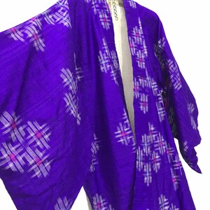 May include: A purple silk kimono with a white and pink geometric pattern. The kimono is hanging on a hanger.
