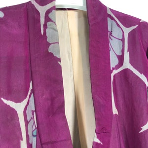 May include: A close-up of the collar of a pink kimono with a white floral pattern. The kimono is hanging on a hanger with the label "AKAGAMI" visible.
