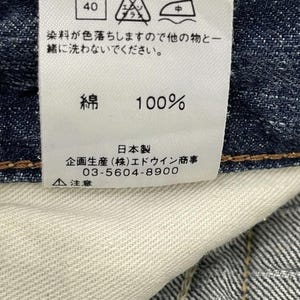 May include: A white clothing tag with care symbols and Japanese text. The tag indicates a 40-degree wash, and the fabric is 100% cotton. The tag also includes the manufacturer's information.