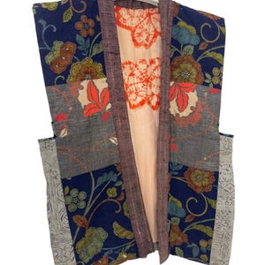 May include: A patchwork kimono-style jacket with a floral pattern in navy blue, gray, and orange. The jacket has a light peach lining with an orange tie-dye design and a dark purple trim. It hangs from a white hanger.