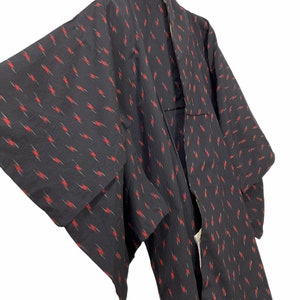 May include: A black kimono with a red and white geometric pattern. The kimono is hanging on a hanger.