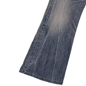 May include: Close-up of a section of blue denim jeans. The jeans have a faded wash effect, with lighter areas creating a worn appearance. Visible are the seams and stitching, with a classic five-pocket design. The denim is a medium weight.