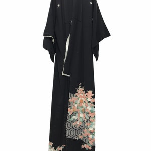 May include: A black kimono with a floral pattern on the bottom hem. The flowers are pink, white, and green. The kimono has a white lining and is hanging on a hanger.