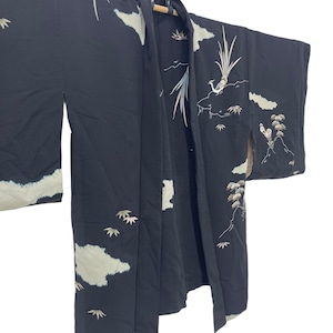 May include: Black kimono with white cloud and bird embroidery. The kimono is hanging from a wooden rod and features a detailed design of birds, clouds, and foliage. The sleeves are long and the fabric appears to be a lightweight material.