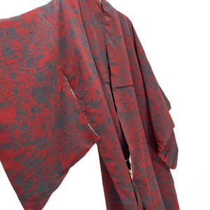 May include: A red and gray kimono with a floral pattern. The kimono is hanging on a hanger.