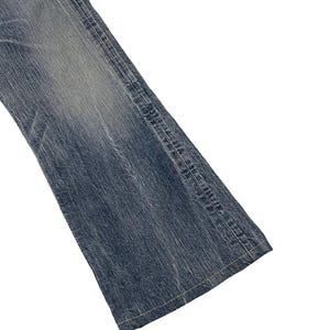 May include: Close-up of a section of blue denim jeans. The jeans have a faded wash and visible stitching along the seams. The fabric appears worn, with subtle variations in color.